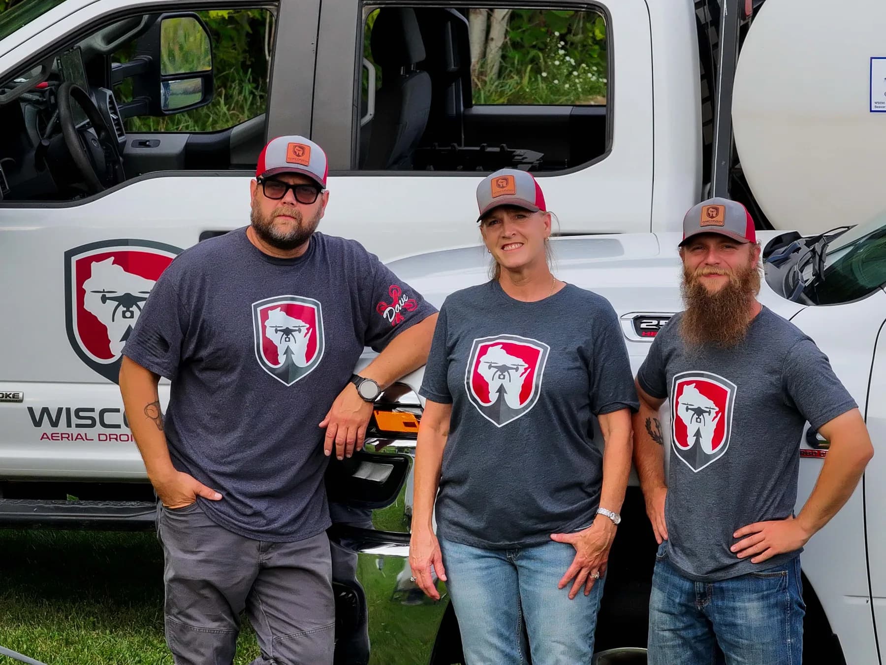 Wisconsin Aerial owners David Lockstein, Chris Lockstein, and Jordan Kurdziel standing together in company shirts beside branded support trucks
