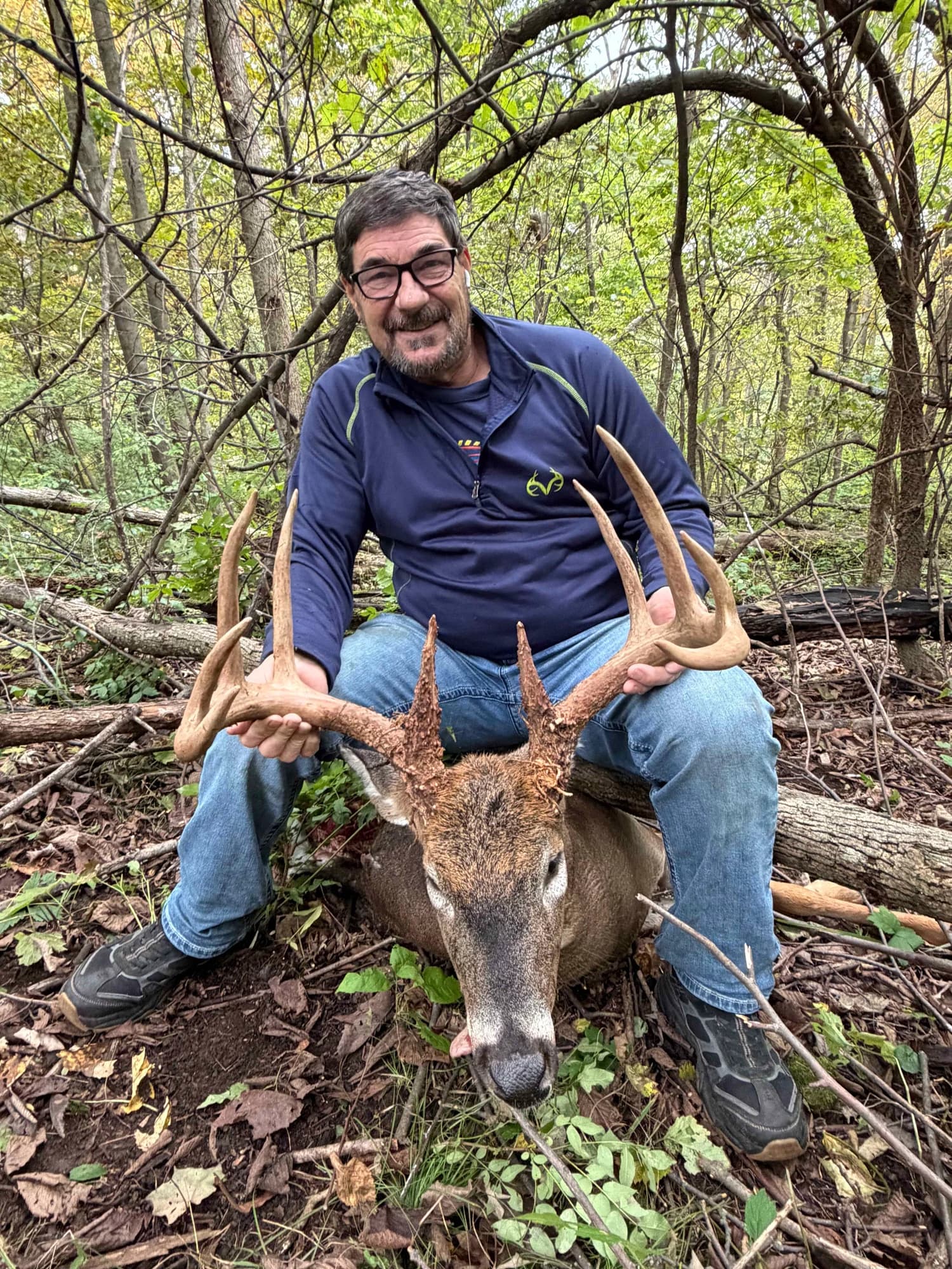 Hunter holding the antlers of a white-tailed buck in a wooded area
